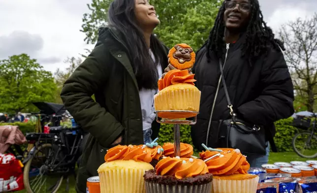 Two girls sell orange pastries during King's Day celebrations in Amsterdam, Netherlands, Saturday, April 27, 2024. (AP Photo/Peter Dejong)