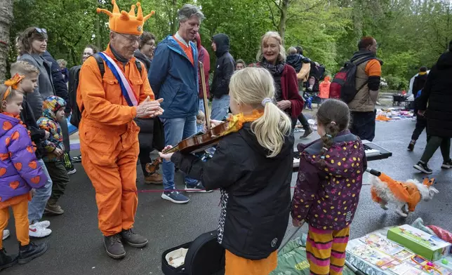 An orange-clad man applauds for a girl playing violin as his orange-clad dog, bottom right corner, runs off during King's Day celebrations in Amsterdam, Netherlands, Saturday, April 27, 2024. (AP Photo/Peter Dejong)
