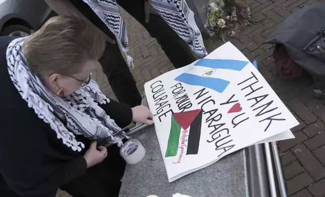 A pro-Palestinian activist works on a protest poster near the International Court of Justice, or World Court, in The Hague, Netherlands, Monday, April 8, 2024, prior to the start of a two days hearing in a case brought by Nicaragua accusing Germany of breaching the genocide convention by providing arms and support to Israel. (AP Photo/Patrick Post)