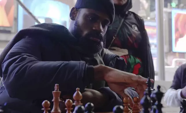 In this screen grab taken from video, Tunde Onakoya, 29- years old, a Nigerian chess champion and child education advocate, play a chess game in Times Square, New York, Thursday, April, 18, 2024. A Nigerian chess player and child education advocate is attempting to play chess nonstop for 58 hours in New York City's Times Square to break the global record for the longest chess marathon and raise $1m for the education of children across Africa. (AP Video/John Minchillo)