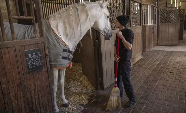 A horsewoman cleans the stables of the royal stables, in Versailles, Thursday, April 25, 2024. More than 340 years after the royal stables were built under the reign of France's Sun King, riders and horses continue to train and perform in front of the Versailles Palace. The site will soon keep on with the tradition by hosting the equestrian sports during the Paris Olympics. Commissioned by King Louis XIV, the stables have been built from 1679 to 1682 opposite to the palace's main entrance. (AP Photo/Aurelien Morissard)
