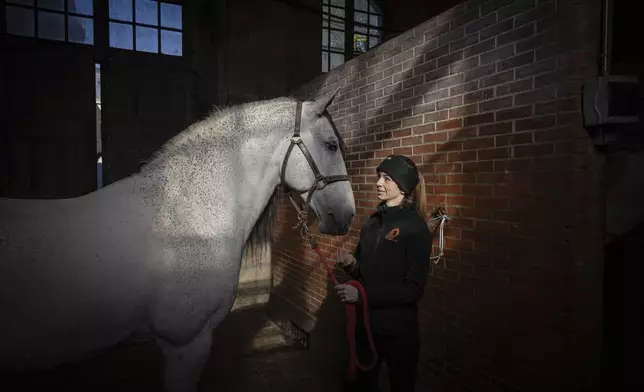 Fanny Lorre, 28, horsewoman at the Académie du Spectacle Equestre poses with her horse in the royal stables, in Versailles, Thursday, April 25, 2024. More than 340 years after the royal stables were built under the reign of France's Sun King, riders and horses continue to train and perform in front of the Versailles Palace. The site will soon keep on with the tradition by hosting the equestrian sports during the Paris Olympics. Commissioned by King Louis XIV, the stables have been built from 1679 to 1682 opposite to the palace's main entrance. (AP Photo/Aurelien Morissard)