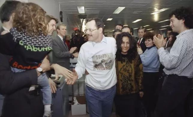 FILE - Wearing a "Hello World" sweatshirt printed with his picture, former hostage Terry Anderson greets happy colleagues, Dec. 10, 1991, at The Associated Press headquarters in New York, as he walks with his arm around fiancée Madeleine Bassil, center right. Anderson, the globe-trotting Associated Press correspondent who became one of America’s longest-held hostages after he was snatched from a street in war-torn Lebanon in 1985 and held for nearly seven years, died Sunday, April 21, 2024. He was 76. (AP Photo/Ron Frehm, File)