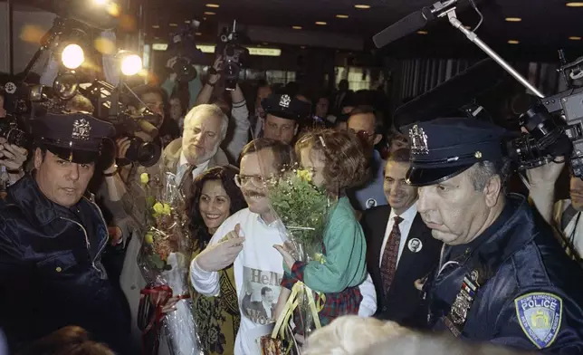 FILE - Former hostage Terry Anderson, center, carries his daughter Sulome, 6, through a crunch of the New York media upon arrival to John F. Kennedy International Airport in New York, Dec. 10, 1991. At left is Sulome's mother, Madeleine Bassil, and at immediate right is Associated Press President Lou Boccardi. Anderson, the globe-trotting AP correspondent who became one of America’s longest-held hostages after he was snatched from a street in war-torn Lebanon in 1985 and held for nearly seven years, died Sunday, April 21, 2024, at age 76. (AP Photo/Ed Bailey, File)