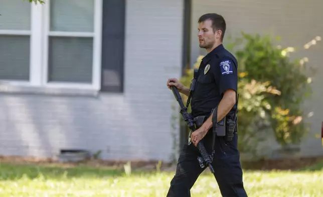A Charlotte Mecklenburg police officer walks carrying a gun in the neighborhood where a shooting took place in Charlotte, N.C., Monday, April 29, 2024. The Charlotte-Mecklenburg Police Department says officers from the U.S. Marshals Task Force were carrying out an investigation Monday afternoon in a suburban neighborhood when they came under gunfire. (AP Photo/Nell Redmond)