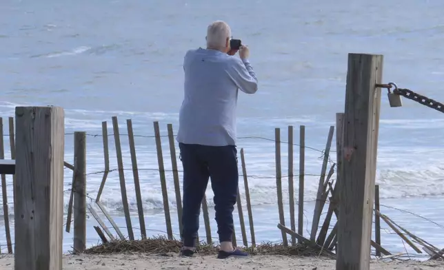 A beachgoer takes photos of the ocean horizon on Thursday, April 25, 2024 in Long Beach Township, N.J. Eight Jersey Shore towns, including Long Beach, are trying to convince New Jersey utility regulators that wind turbines planned for less than 9 miles off the town's coast will scare away visitors, costing the area jobs and economic development. The wind power industry rejects those claims, and says turbines can coexist with tourism and fishing. (AP Photo/Wayne Parry)