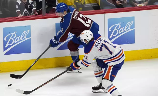 Colorado Avalanche right wing Brandon Duhaime, back, slips the puck past Edmonton Oilers center Ryan McLeod during the first period of an NHL hockey game Thursday, April 18, 2024, in Denver. (AP Photo/David Zalubowski)