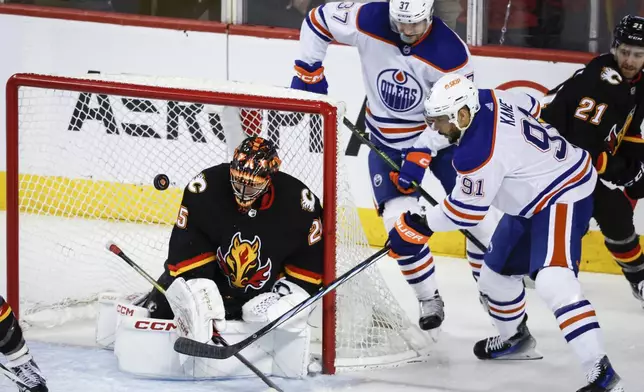 Edmonton Oilers forward Evander Kane (91) tries to score on Calgary Flames goalie Jacob Markstrom (25) as forward Warren Foegele (37) watches during the third period of an NHL hockey game Saturday, April 6, 2024, in Calgary, Alberta. (Jeff McIntosh/The Canadian Press via AP)