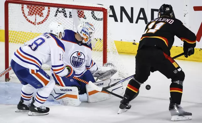 Edmonton Oilers goalie Calvin Pickard (30) kicks away a shot from Calgary Flames forward Mikael Backlund (11) as forward Zach Hyman (18) watches during the second period of an NHL hockey game Saturday, April 6, 2024, in Calgary, Alberta. (Jeff McIntosh/The Canadian Press via AP)