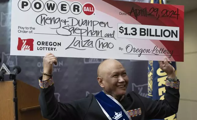 Cheng "Charlie" Saephan holds display check above his head after speaking during a news conference where it was revealed that he was one of the winners of the $1.3 billion Powerball jackpot at the Oregon Lottery headquarters on Monday, April 29, 2024, in Salem, Ore. (AP Photo/Jenny Kane)