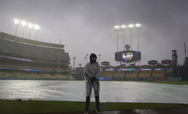 A security guard stands on the field in the rain before of a baseball game between the Los Angeles Dodgers and the San Diego Padres, Saturday, April 13, 2024, in Los Angeles. (AP Photo/Marcio Jose Sanchez)