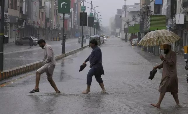 People cross a road during heavy rain in Peshawar, Pakistan, Monday, April 15, 2024. Lightening and heavy rains killed dozens of people, mostly farmers, across Pakistan in the past three days, officials said Monday, as authorities declared a state of emergency in the country's southwest following an overnight rainfall to avoid any further casualties and damages. (AP Photo/Muhammad Sajjad)