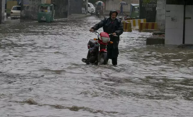A Pakistani with his bike wades through a flooded road caused by heavy rain in Peshawar, Pakistan, Monday, April 15, 2024. Lightening and heavy rains killed dozens of people, mostly farmers, across Pakistan in the past three days, officials said Monday, as authorities declared a state of emergency in the country's southwest following an overnight rainfall to avoid any further casualties and damages. (AP Photo/Muhammad Sajjad)