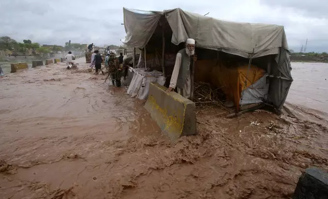 People stand beside a make shift stall set up on the bank of a stream, which is overflowing following heavy rains, on the outskirts of Peshawar, Pakistan, Monday, April 15, 2024. Lightnings and heavy rains killed dozens of people, mostly farmers, across Pakistan in the past three days, officials said Monday, as authorities declared a state of emergency in the country's southwest following an overnight rainfall to avoid any further casualties and damages. (AP Photo/Muhammad Sajjad)