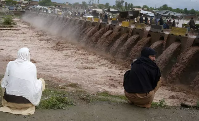 People looks a stream, which is overflowing following heavy rains, on the outskirts of Peshawar, Pakistan, Monday, April 15, 2024. Lightnings and heavy rains killed dozens of people, mostly farmers, across Pakistan in the past three days, officials said Monday, as authorities declared a state of emergency in the country's southwest following an overnight rainfall to avoid any further casualties and damages. (AP Photo/Muhammad Sajjad)