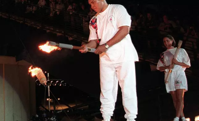 FILE - American swimmer Janet Evans, right, looks on as Muhammad Ali lights the Olympic flame during the 1996 Summer Olympic Games opening ceremony in Atlanta, July 19, 1996. On Tuesday, April 16, 2024 the flame for this summer's Paris Olympics will be lit and be carried through Greece for more than 5,000 kilometers (3,100 miles) before being handed over to French organizers at the Athens site of the first modern Olympics. (AP Photo/Michael Probst, File)