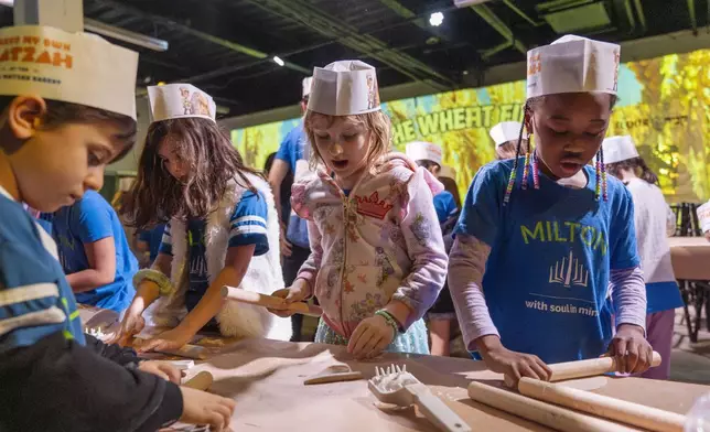 Hana Chmeruk, center, who moved to the U.S. from Ukraine, and Avigael Yahyisrael, 7, make matzah with other first graders from Milton Gottesman Jewish Day School of the Nation's Capital, during a "Matzah Factory" field trip to the JCrafts Center for Jewish Life and Tradition in Rockville, Md., Thursday, April 18, 2024, ahead of the Passover holiday which begins next Monday evening. To be kosher for Passover the dough has to be prepared and cooked all within 18 minutes and not allowed to rise. (AP Photo/Jacquelyn Martin)