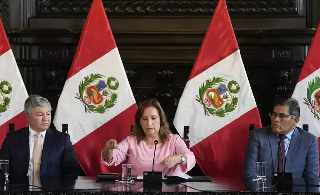 Peru's President Dina Boluarte shows her necklace, accompanied by her lawyers Mateo Castaneda, left, and Eduardo Barriga, during a press conference at Government Palace in Lima, Peru, Friday, April 5, 2024. Authorities are investigating on whether she illegally received hundreds of thousands of dollars in cash, luxury watches and jewelry. (AP Photo/Martin Mejia)