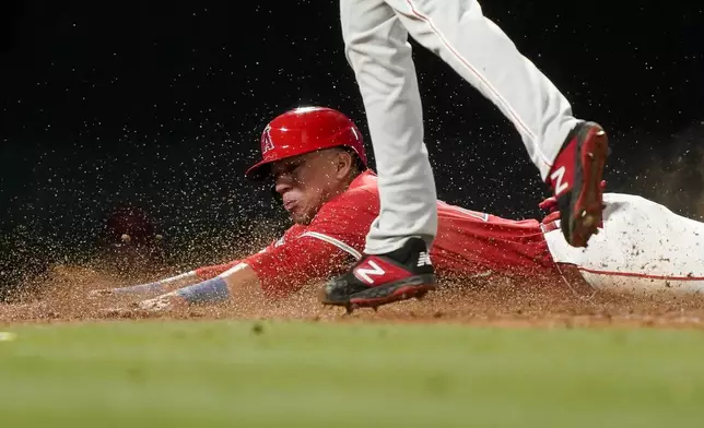 Los Angeles Angels' Ehire Adrianza, bottom, slides past Philadelphia Phillies relief pitcher Seranthony Dominguez to score on a wild pitch during the seventh inning of a baseball game, Monday, April 29, 2024, in Anaheim, Calif. Mike Trout also scored after a throwing error by Phillies catcher Garrett Stubbs. (AP Photo/Ryan Sun)