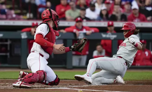 Philadelphia Phillies' Alec Bohm, right, safely slides into home to score on a sacrifice fly by teammate Bryson Scott as Cincinnati Reds catcher Tyler Stephenson, left, looks to tag in the second inning of a baseball game on Monday, April 22, 2024, in Cincinnati. (AP Photo/Carolyn Kaster)