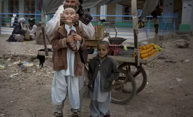 FILE - A fruit seller lifts his son by his cheeks in the center of Kandahar, Afghanistan, Wednesday, March 12, 2014. (AP Photo/Anja Niedringhaus, File)