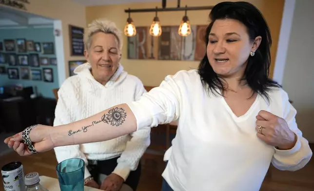 Shannon Rodriguez, right, shows off a tattoo made of her mother Deb Robertson's handwriting "Love You More" and sunflower at Robertson's Lombard, Ill., home Saturday, March 23, 2024. Robertson didn’t cry when she learned two months ago that the cancerous tumors in her liver were spreading, portending a tormented death. But later, she cried after receiving a call that a bill moving through the Illinois Legislature to allow certain terminally ill patients to end their own lives with a doctor’s help had made progress. (AP Photo/Charles Rex Arbogast)