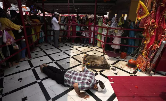 A Hindu devotee prostrates as others stand in a queue to offer prayers inside the historical Kali Temple, situated inside Bahu Fort, on the fifth day of the Navratri, or nine nights festival, in Jammu, India, Saturday, April.13, 2024. Navaratri lasts for nine days, with three days each devoted to the worship of the goddess of valor Durga, the goddess of wealth Lakshmi, and the goddess of knowledge Saraswati. (AP Photo/Channi Anand)
