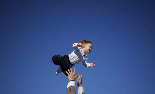 A Muslim man playfully throws a baby in the air at the end of Eid al-Fitr prayers in Bucharest, Romania, Wednesday, April 10, 2024. (AP Photo/Andreea Alexandru)