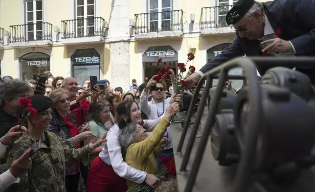 Celeste Caeiro, 90, hands red carnations to former army captain Manuel Correia Silva, in Lisbon, Thursday, April 25, 2024, during the reenactment of troops movements of fifty years ago, part of anniversary celebrations of the Carnation Revolution. (AP Photo/Ana Brigida)