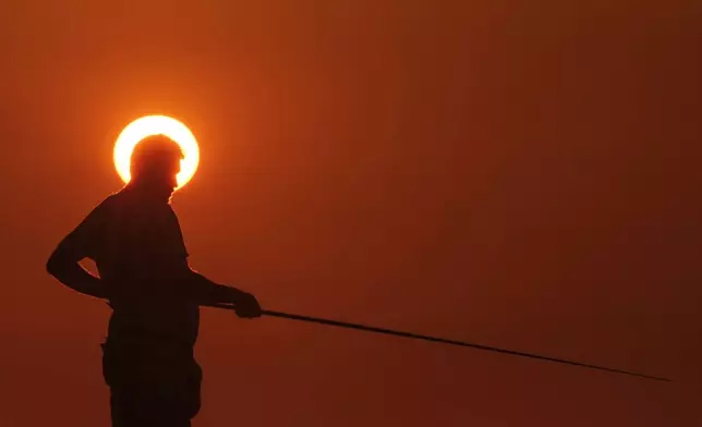 A fisherman is silhouetted against a setting sun as he fishes from a rocky area along the Beirut coastline, in Lebanon, April 15, 2024. (AP Photo/Hassan Ammar)