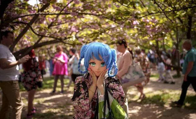 A woman wearing a sweet girl cosplay mask strikes a pose during a flower watching or Hanami event, in the Japanese Garden of Bucharest, Romania, April 13, 2024. (AP Photo/Andreea Alexandru)