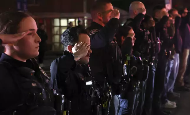 Police officers salute as the bodies of two officers are transported to the Wally Howard Forensics Science Center in Syracuse, N.Y., Monday, April 15, 2024. Police officers from several local agencies gathered at Upstate hospital's emergency room to hear the news of the slain officers. (Dennis Nett/The Post-Standard via AP)