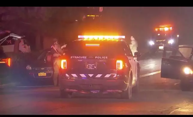 Armed law enforcement officers patrol around the scene of a shooting in Liverpool, N.Y., Sunday, April 14, 2024. A police officer and a sheriff's deputy in upstate New York were shot and killed Sunday night in an exchange of gunfire with a suspect, who also was killed, police said. (WSYR-TV Syracuse via AP)