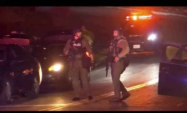 Armed law enforcement officers patrol around the scene of a shooting in Liverpool, N.Y., Sunday, April 14, 2024. A police officer and a sheriff's deputy in upstate New York were shot and killed Sunday night in an exchange of gunfire with a suspect, who also was killed, police said. (WSYR-TV Syracuse via AP)