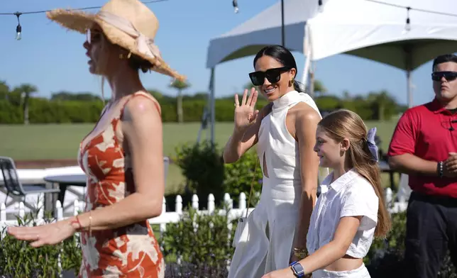 Meghan Markle, Duchess of Sussex, waves to the press as she walks with Delfina Blaquier, left, and Alba Figueras, the wife and daughter of Argentine professional polo player Ignacio "Nacho" Figueras, as she arrives for the 2024 Royal Salute Polo Challenge to Benefit Sentebale, Friday, April 12, 2024, in Wellington, Fla. Prince Harry, co-founding patron of the Sentebale charity, will play on the Royal Salute Sentebale Team. (AP Photo/Rebecca Blackwell)