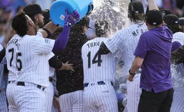 Colorado Rockies catcher Elias Díaz, far left, dumps water onto teammates as they mob Ryan McMahon, who crosses home plate after hitting a grand slam off Tampa Bay Rays pitcher Jason Adam during the ninth inning of a baseball game Friday, April 5, 2024, in Denver. (AP Photo/David Zalubowski)