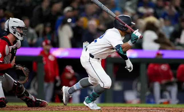 Seattle Mariners' Jonatan Clase follows through on an RBI single for his first major league hit as Cincinnati Reds catcher Tyler Stephenson, left, looks on during the sixth inning of a baseball game Monday, April 15, 2024, in Seattle. (AP Photo/Lindsey Wasson)