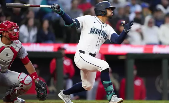 Seattle Mariners' Jonatan Clase follows through on an RBI double next to Cincinnati Reds catcher Luke Maile during the fourth inning of a baseball game Tuesday, April 16, 2024, in Seattle. (AP Photo/Lindsey Wasson)
