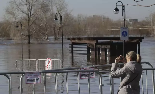 A woman takes a photo of a flooded area next to Ural river in Orenburg, Russia, on Thursday, April 11, 2024. Russian officials are scrambling to help homeowners displaced by floods, as water levels have risen in the Ural River. The river's water level in the city of Orenburg was above 10 meters (33 feet) Wednesday, state news agency Ria Novosti reported, citing the regional governor. (AP Photo)