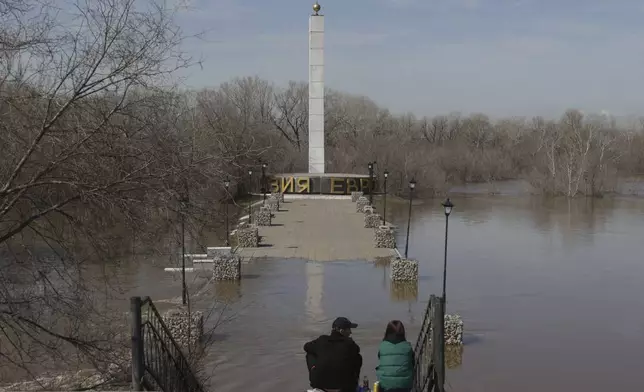 A couple sits on stairs watching a flooded area around the Stele Europe - Asia, showing the border between Europe and Asia, in Orenburg, Russia, on Thursday, April 11, 2024. Russian officials are scrambling to help homeowners displaced by floods, as water levels have risen in the Ural River. The river's water level in the city of Orenburg was above 10 meters (33 feet) Wednesday, state news agency Ria Novosti reported, citing the regional governor. (AP Photo)