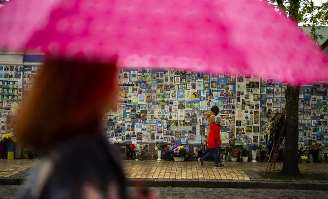 People walk past a memorial wall with photographs of Ukrainian soldiers killed during the war, at Saint Michael cathedral during a rainy morning in Kiev, Ukraine, Sunday, April 21, 2024. The House swiftly approved $95 billion in foreign aid for Ukraine, Israel and other U.S. allies in a rare Saturday session as Democrats and Republicans banded together after months of hard-right resistance over renewed American support for repelling Russia's invasion. (AP Photo/Francisco Seco)