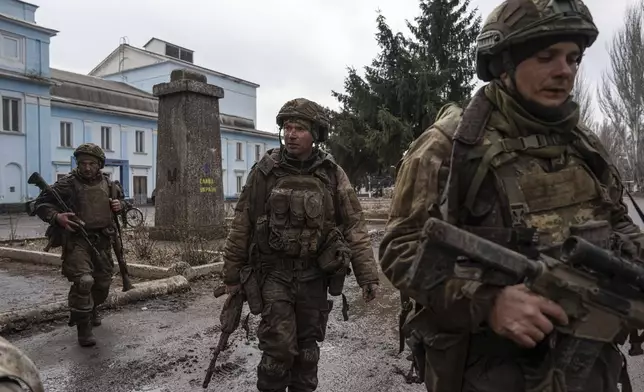 FILE - Ukrainian servicemen who recently returned from the trenches of Bakhmut walk on a street in Chasiv Yar, Ukraine, Wednesday, March 8, 2023. Approval by the U.S. House of a $61 billion package for Ukraine puts the country a step closer to getting an infusion of new firepower. But the clock is ticking. Russia is using all its might to achieve its most significant gains since the invasion by a May 9 deadline. (AP Photo/Evgeniy Maloletka, File)