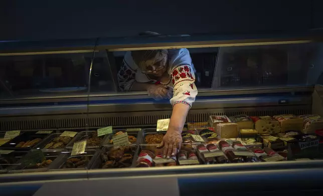 A saleswoman places goods in a refrigerator in a store that runs on a generator after the municipality temporarily cut the power to conserve energy in Kharkiv, Ukraine, on Sunday, April 14, 2024. (AP Photo/Evgeniy Maloletka)