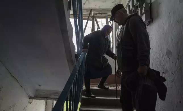 FILE - A volunteer helps Olha Faichuk, 79, down the stairs from her apartment, which was heavily damaged by a Russian airstrike, in Lukiantsi, Kharkiv region, Ukraine, on Tuesday, April 16, 2024. (AP Photo/Evgeniy Maloletka, File)