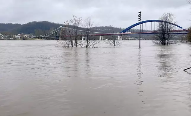 The Ohio River floods its banks, Thursday, April 4, 2024, in Wheeling, W.Va., following days of heavy rains in the region. The Wheeling Suspension Bridge can be seen in the background. (John McCabe/The Intelligencer via AP)