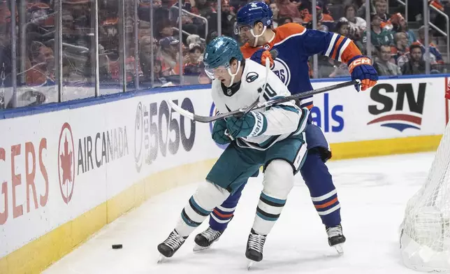 San Jose Sharks' Klim Kostin (10) and Edmonton Oilers' Evan Bouchard (2) battle for the puck during the first period of an NHL hockey game in Edmonton, Alberta, on Monday, April 15, 2024. (Jason Franson/The Canadian Press via AP)