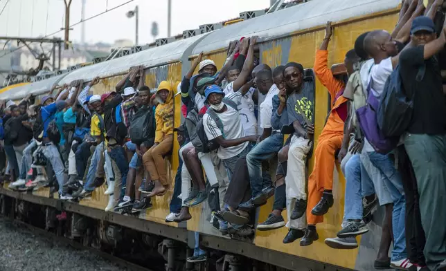 FILE - Train commuters hold on to the side of an overcrowded passenger train in Soweto, South Africa. Monday, March 16, 2020. South Africans celebrate "Freedom Day" every April 27, when they remember their country's pivotal first democratic elections in 1994 that announced the official end of the racial segregation and oppression of apartheid.(AP Photo/Themba Hadebe, File)