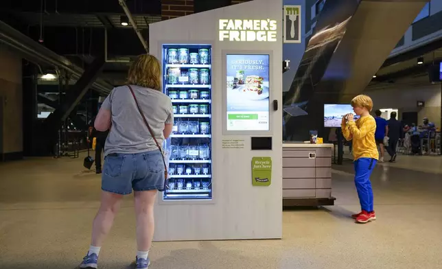 A fan looks at the Farmer's Fridge food vending machine on the ballpark concourse at Globe Life Field before a spring training baseball game between the Texas Rangers and the Boston Red Sox, Monday, March 25, 2024, in Arlington, Texas. Most parks and arenas have a handful of areas that offer salads, gluten free or vegan offerings if fans are willing to hunt a little. But the vast majority of people attending baseball games aren't necessarily looking to eat healthy. (AP Photo/Sam Hodde)