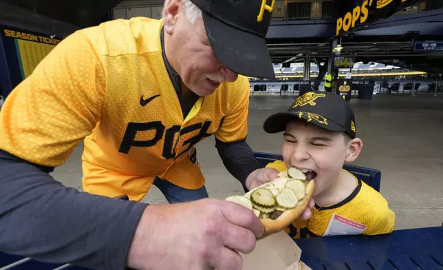 Tim Suwinski, father of Pittsburgh Pirates' Jack Suwinski, and grandson Will Hackl, both of Chicago, share a Renegade hot dog before a baseball game between the Pirates and the Boston Red Sox in Pittsburgh, Friday, April 19, 2024. (AP Photo/Gene J. Puskar)