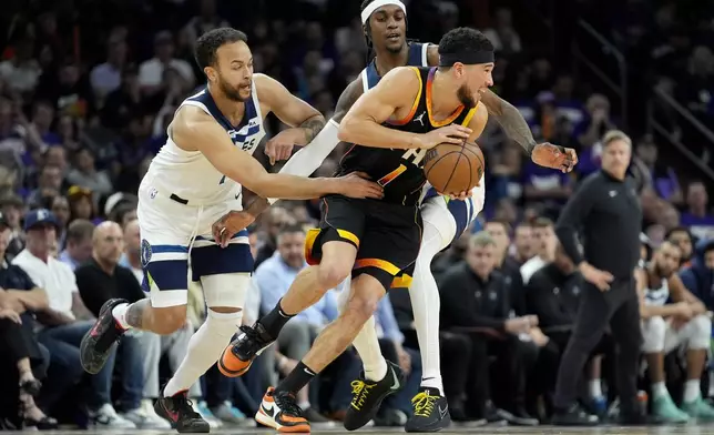 Minnesota Timberwolves forward Kyle Anderson, left, and forward Jaden McDaniels, center, pressure Phoenix Suns guard Devin Booker during the first half of Game 3 of an NBA basketball first-round playoff series, Friday, April 26, 2024, in Phoenix. (AP Photo/Matt York)